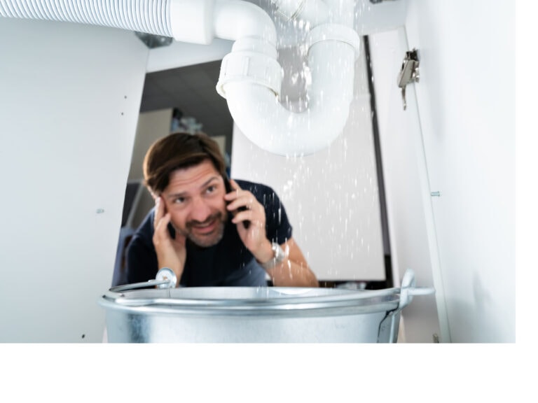 Man under a drain on phone calling for assistance.