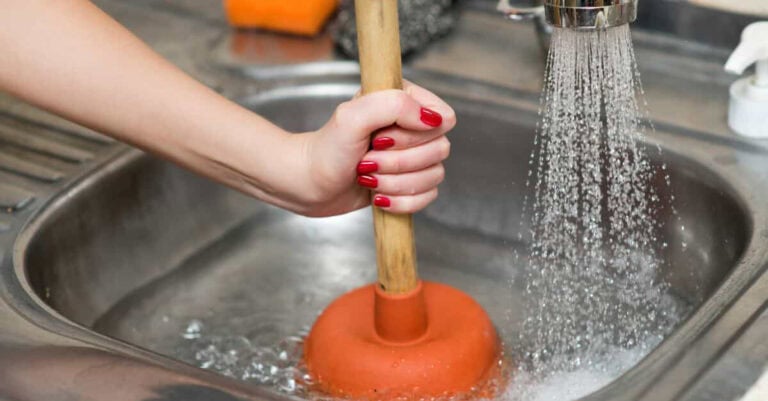 An individual unclogging a drain with a plungger.