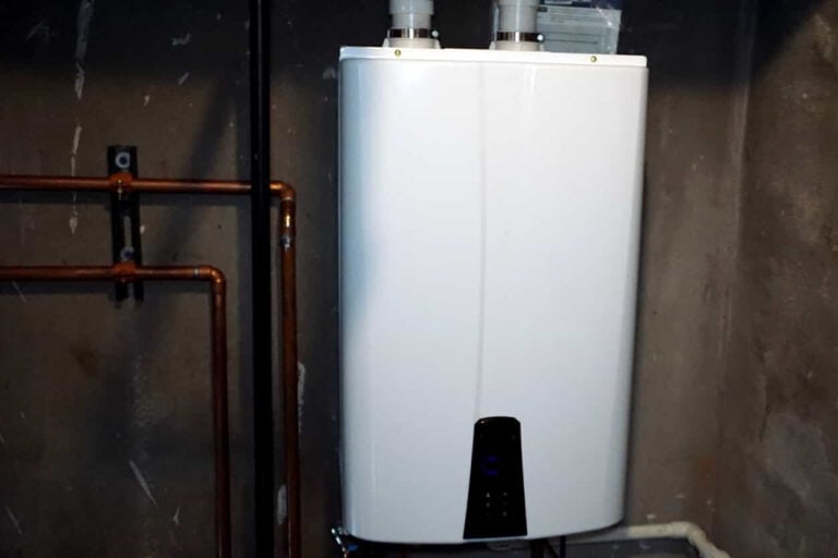 A white tank-style water heater with copper pipes connected to it, mounted on a wall in a basement.