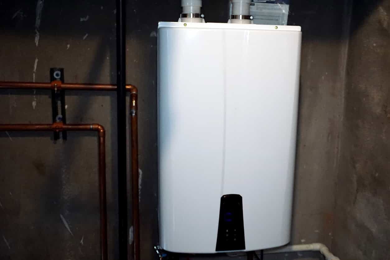 A white tank-style water heater with copper pipes connected to it, mounted on a wall in a basement.